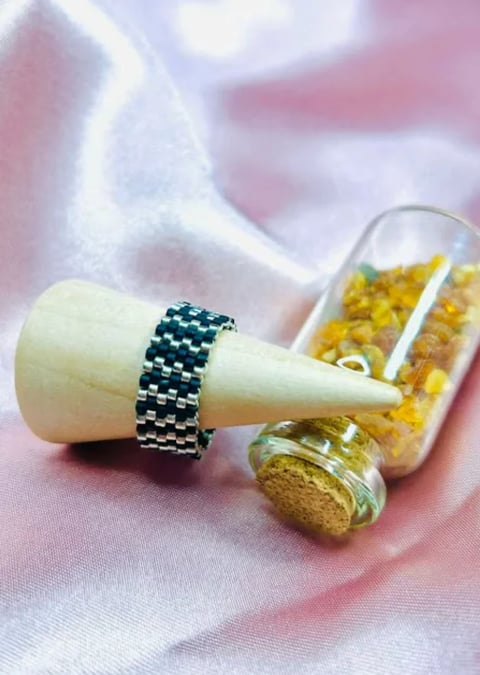 Wooden mortar and pestle with navy beaded ring beside glass bottles of yellow spices on pink fabric