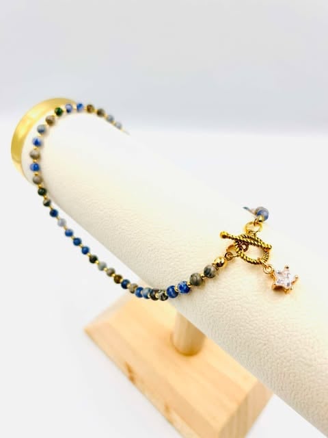 Beaded bracelet with gold clasp and pendant displayed on cream-colored fabric stand against white background