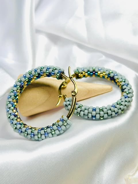 Pair of beaded hoop earrings with blue and green seed beads and gold-tone hooks on white fabric