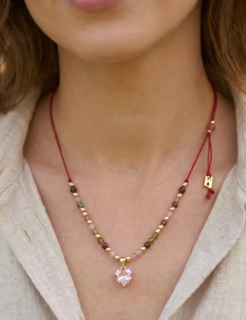 Woman wearing a beaded necklace with a pink crystal pendant and adjustable string closure