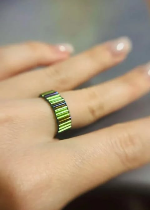 Hand wearing a neon green and black striped ring on the middle finger with polished nails